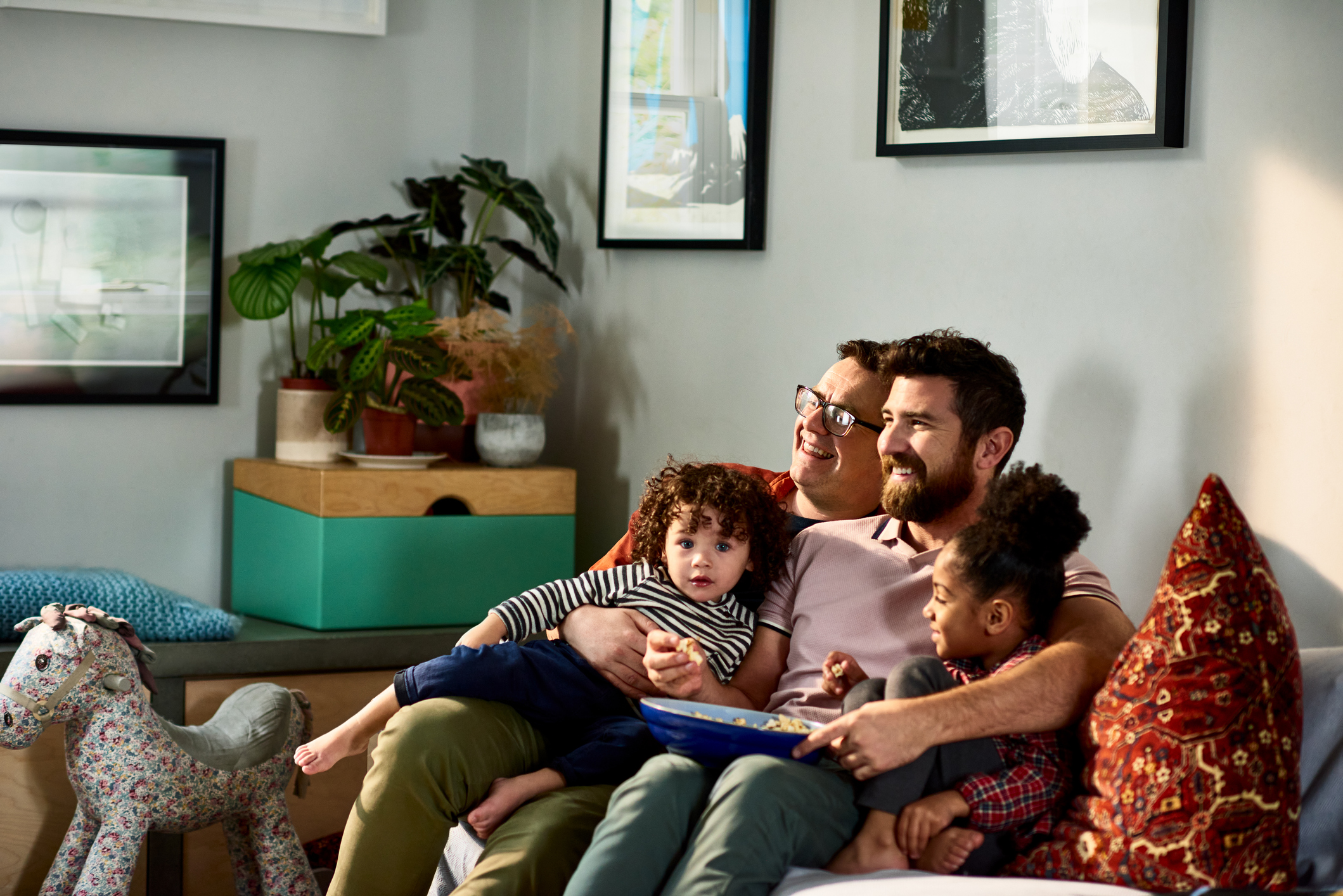 Gay fathers with two young children in living room, watching television, lockdown, relaxation, lifestyles